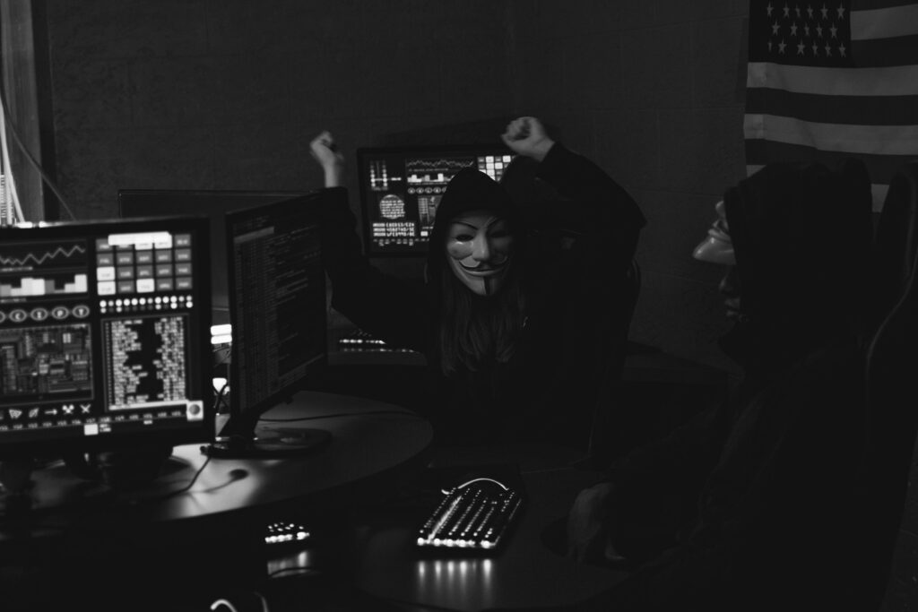 Hacker group with masks celebrating a successful cyber attack in a dimly lit room.